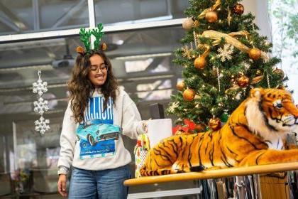 一个学生站在一棵圣诞树旁边，圣诞树前面放着一只玩具老虎